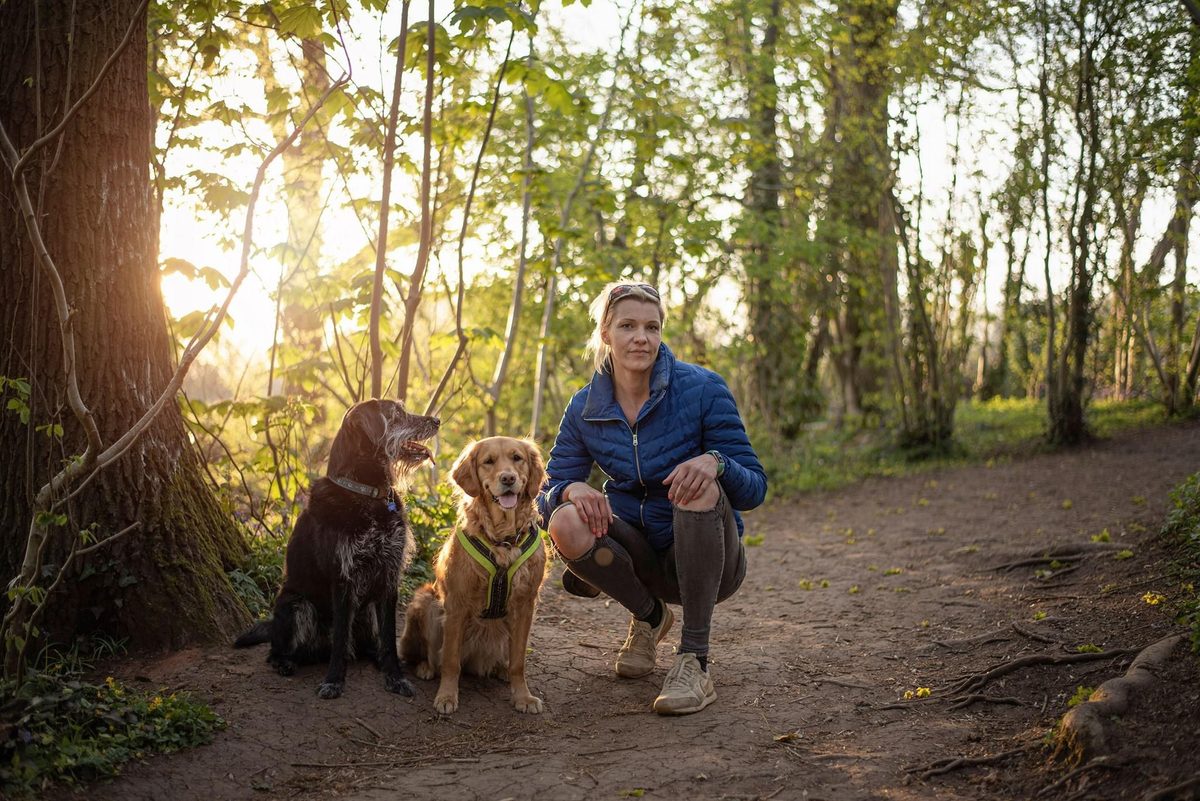 Julia crouching on a woodland path at golden hour with Ludo and Georgie sitting beside her
